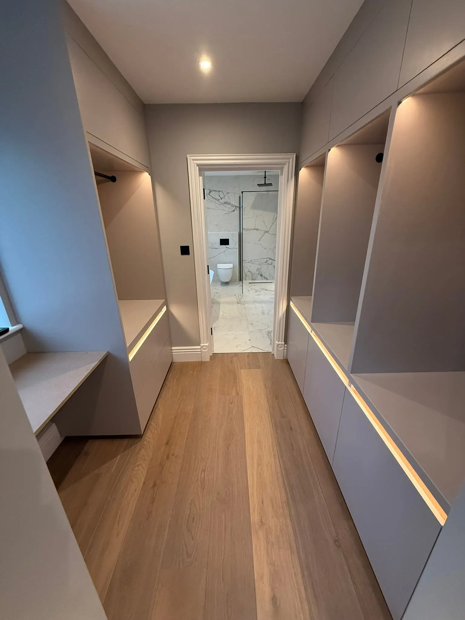 Walk-through dressing room with grey wardrobes lit by LED strips