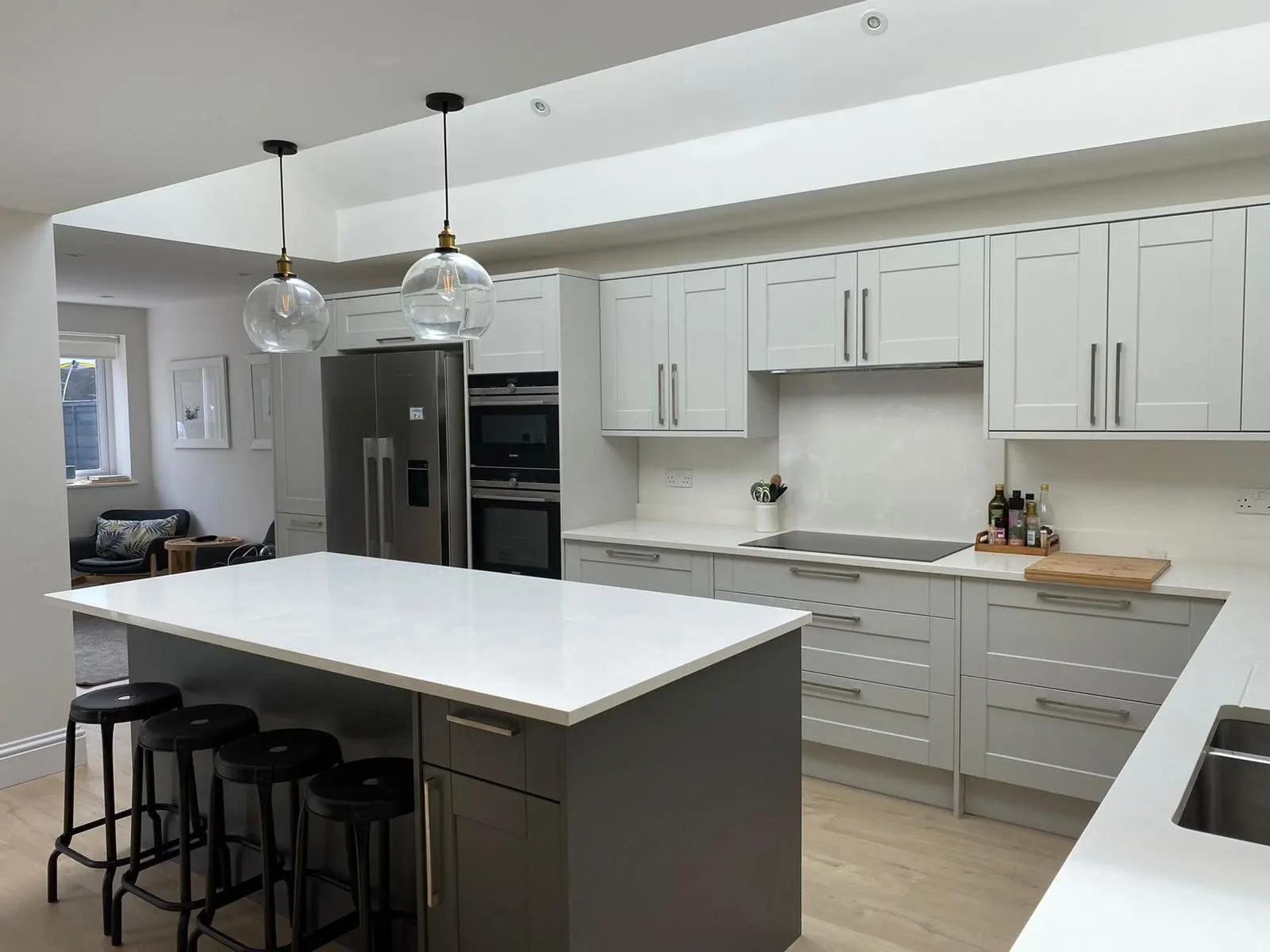 Kitchen with pale grey shaker units, a white stone island and two glass pendant lights, Weybridge