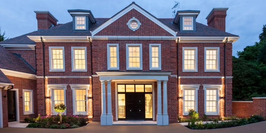 The same house built: red brick with stone window surrounds and a columned porch, lit at dusk, Kingston