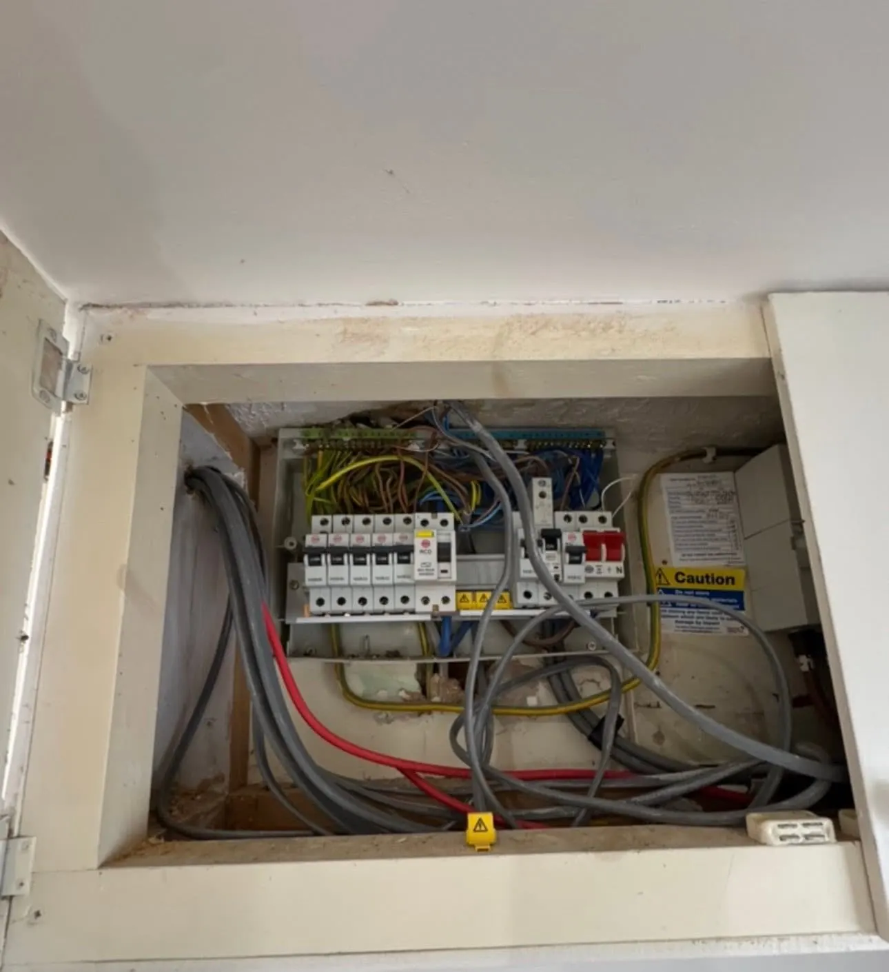 The old fuse board in its cupboard, cover off, with a tangle of cables