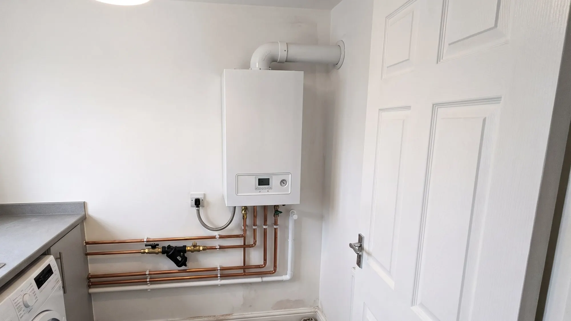 A new wall-hung boiler in a utility room, with its copper pipework, valves and flue