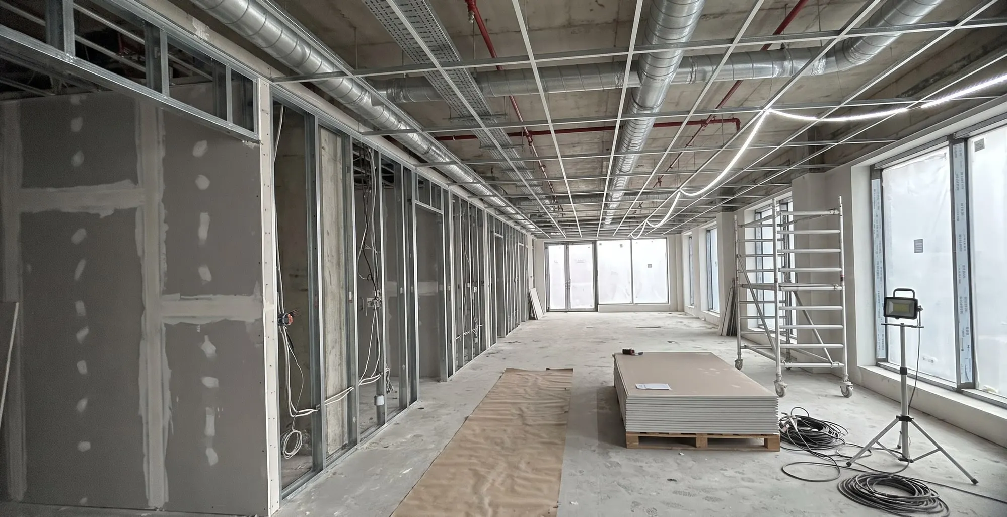 Commercial unit part-way through fit-out: metal stud partitions, ceiling services and a tower scaffold