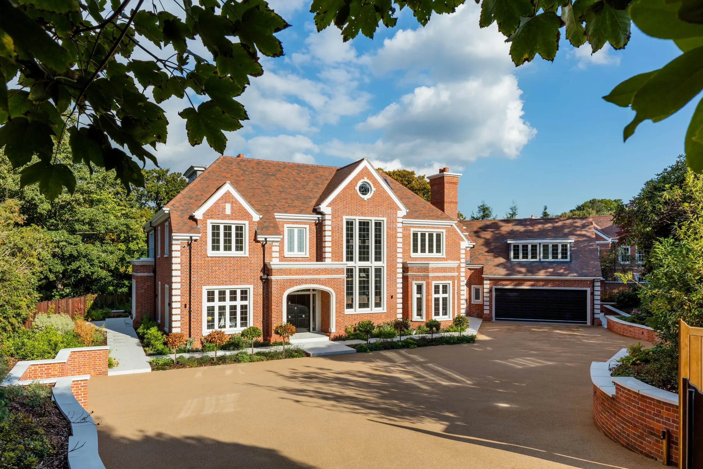 The front of a large brick house with stone quoins, seen across its drive on a bright day