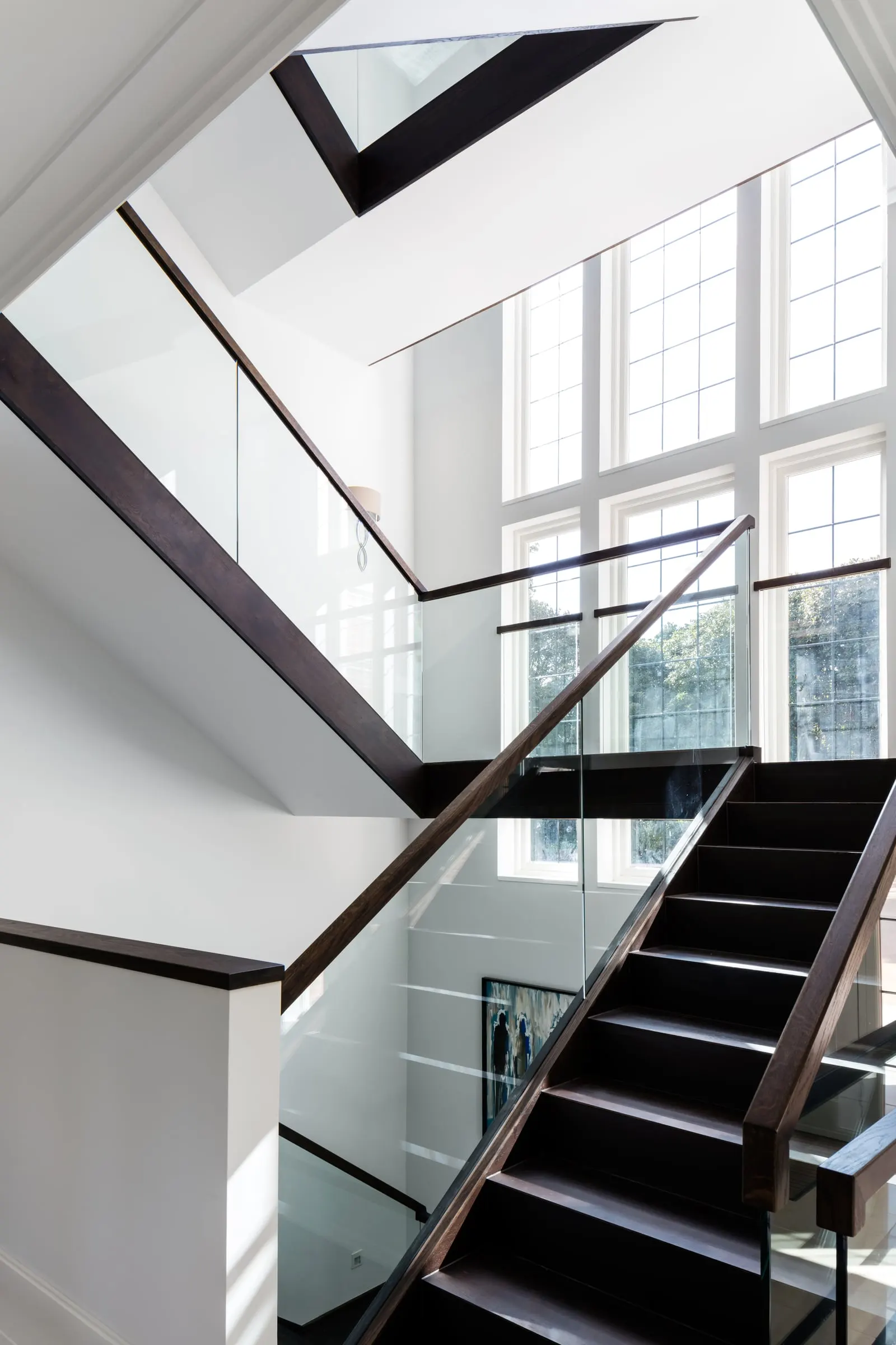 Stairwell with glass balustrades and dark timber handrails beside a tall leaded window