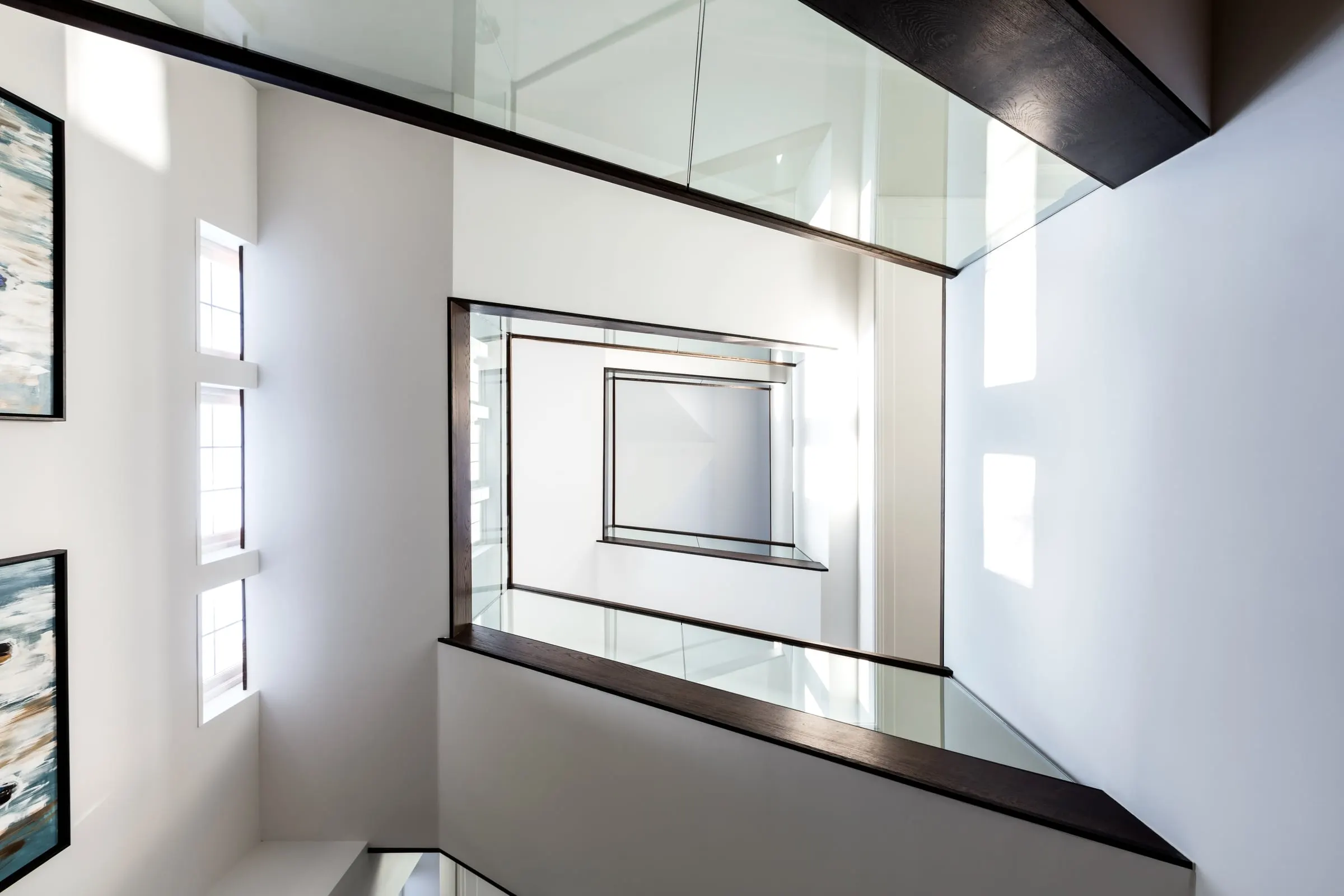 Looking up a stairwell at glass balustrades edged in dark timber
