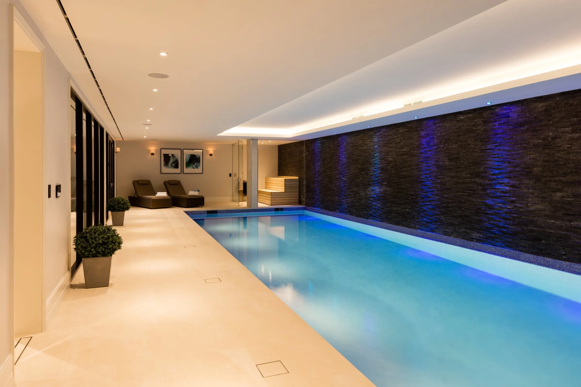 Indoor pool with a slate wall washed in blue light and a pale stone floor