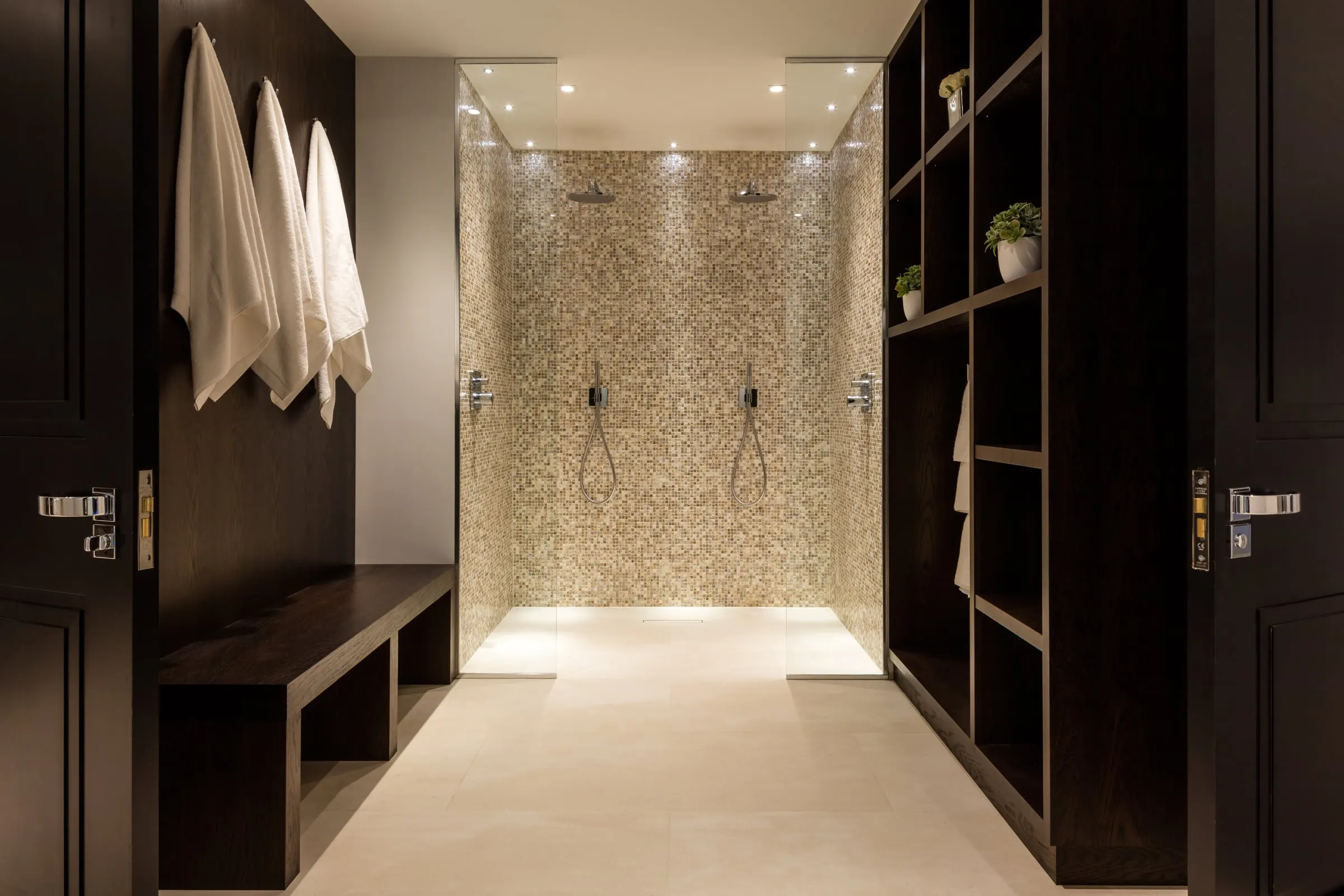 Mosaic-tiled twin shower seen through dark timber doors
