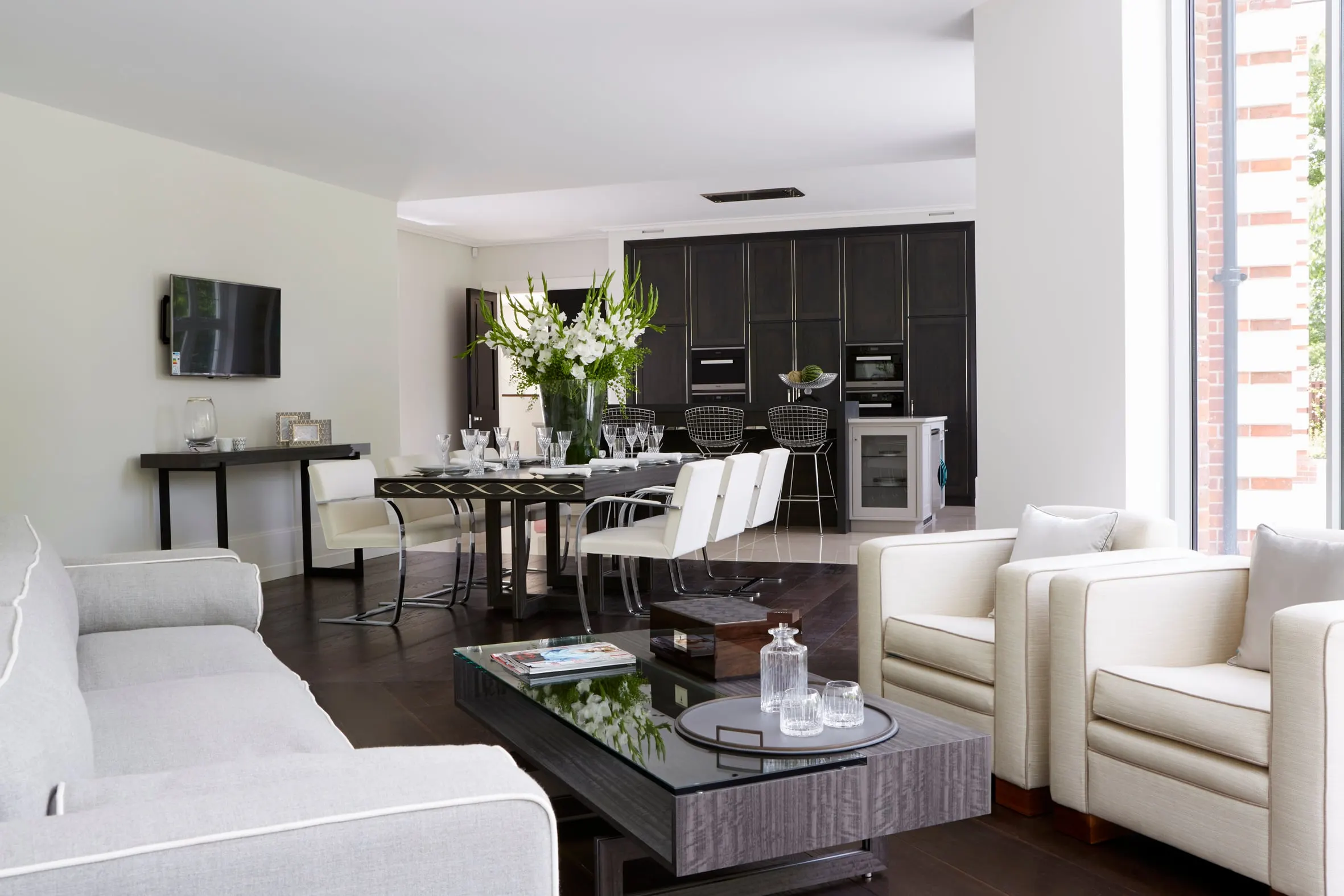 Finished open-plan room: a dining table set for a meal, cream armchairs and a dark oak kitchen behind