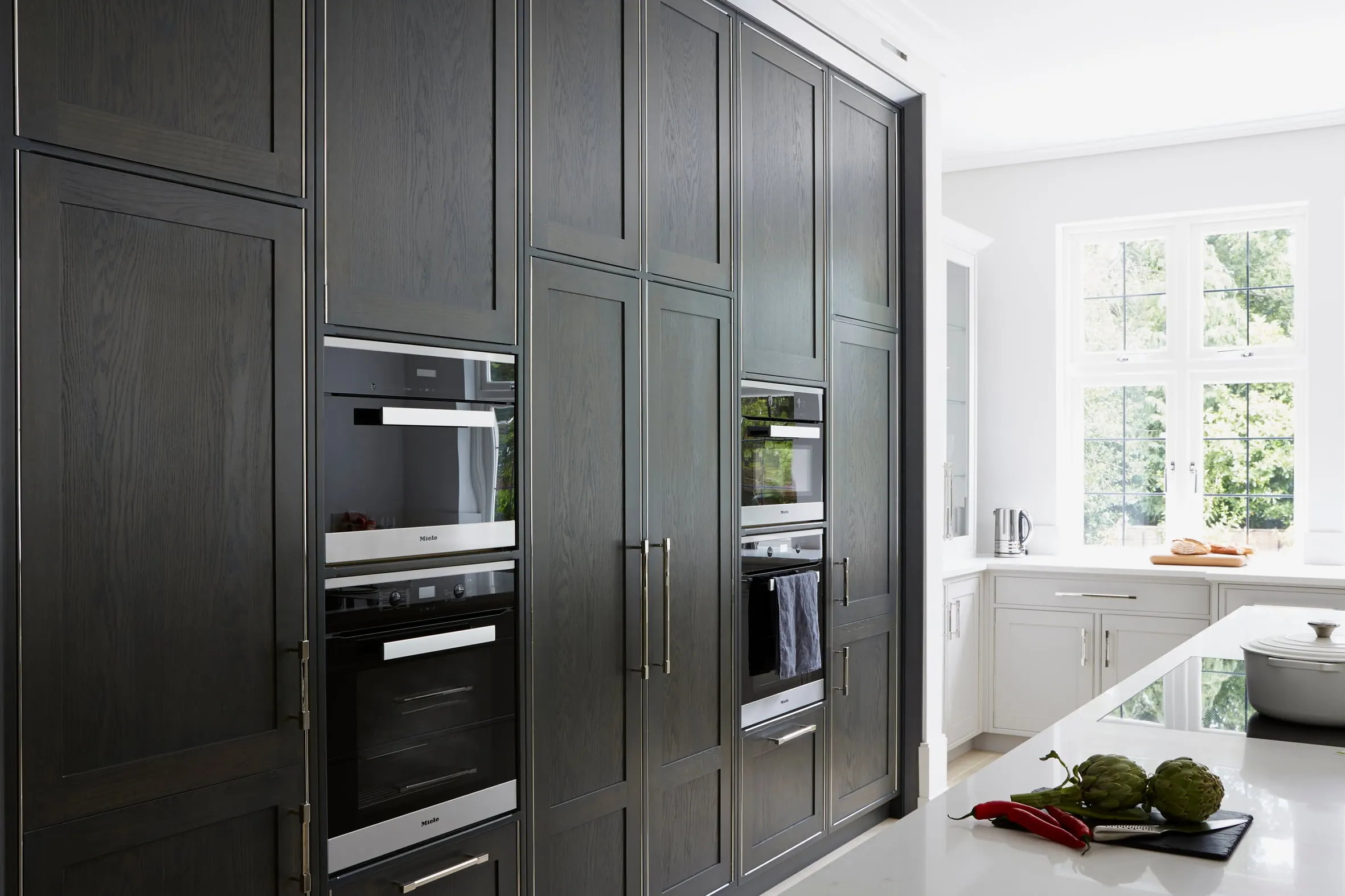 Dark oak tall units with built-in ovens beside a white stone worktop, Kingston