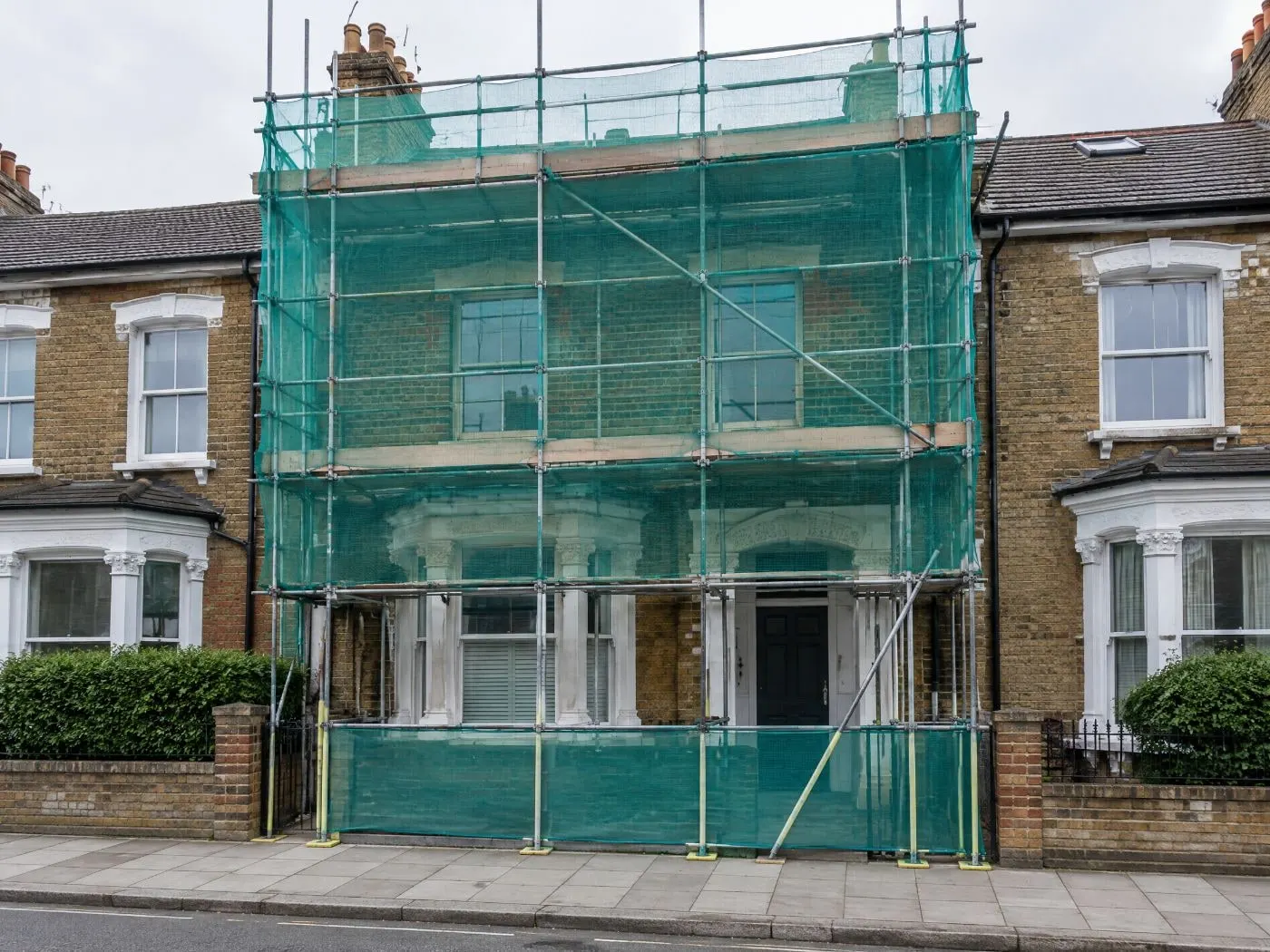 Terraced house scaffolded and sheeted while the work goes on behind
