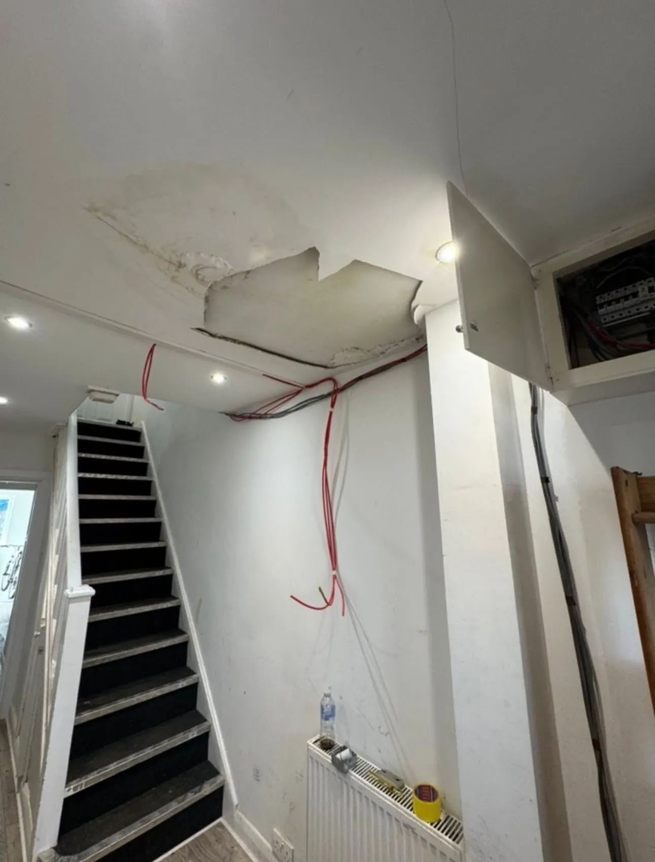 A hall ceiling stained and broken through by a leak from the roof, with cables hanging loose