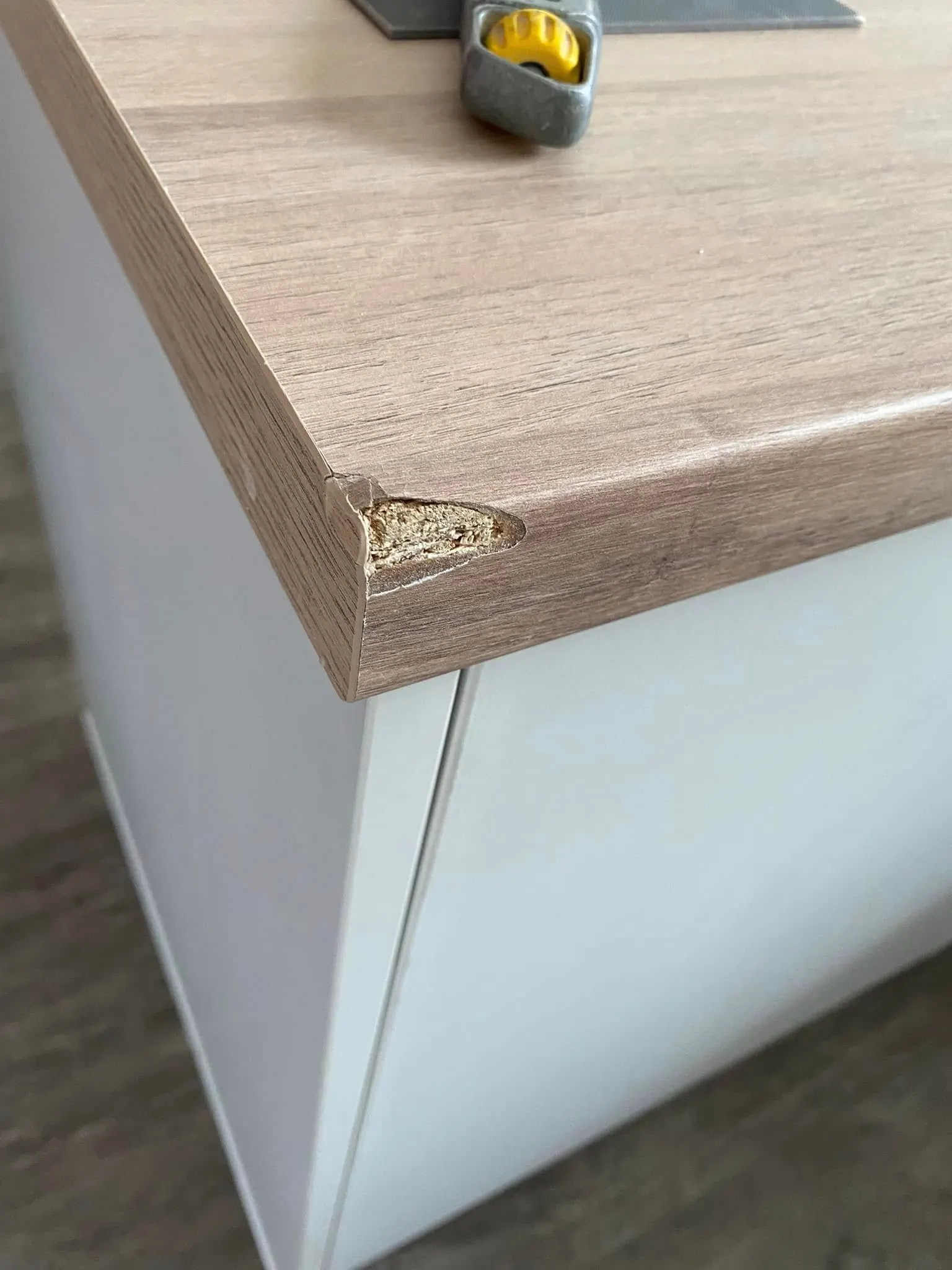 Chipped corner of a laminate worktop, with a filler gun standing ready