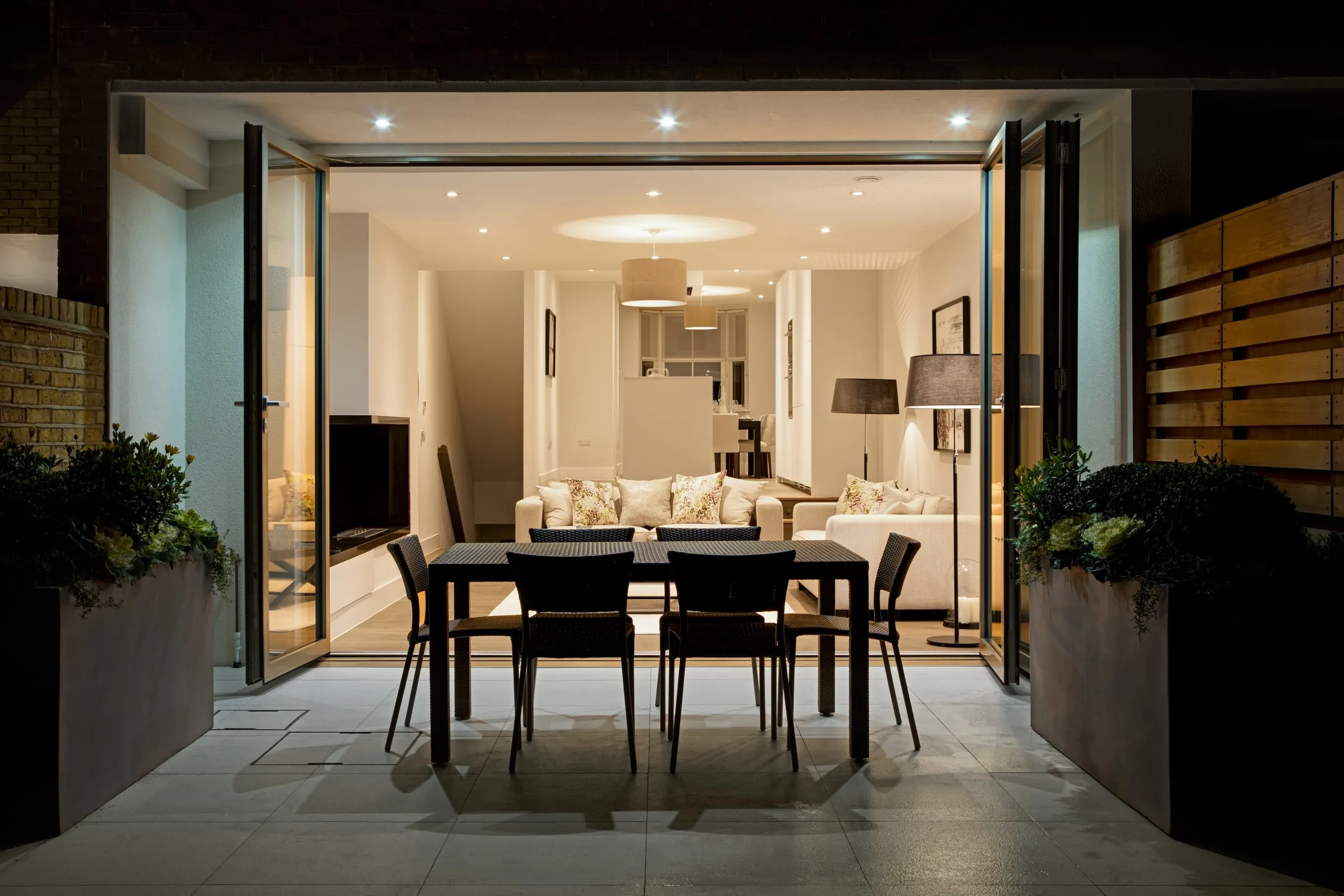 Evening view from the terrace through open doors into a lit living room, Teddington